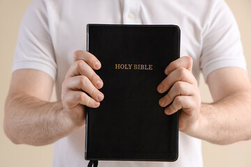 Young man with Holy Bible praying on beige background, closeup