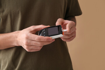 Diabetic young man using glucometer on beige background, closeup