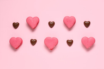 Tasty heart-shaped macaroons and chocolate candies on pink background. Valentine's Day celebration