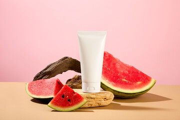 Front view of an empty cosmetic tube without label placed on a stone platform with fresh watermelon on a pink background. Cosmetics advertising with copy space.