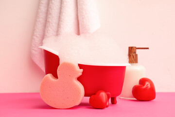Mini bathtub with soap foam, bath supplies and hearts on color background. Valentine's Day celebration