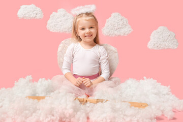 Cute little girl dressed as cupid with bow, arrow and clouds sitting on pink background. Valentine's Day celebration