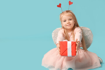 Cute little girl dressed as cupid with gift box sitting on blue background. Valentine's Day...