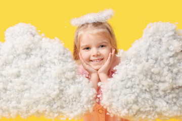 Cute little girl dressed as cupid with clouds on yellow background. Valentine's Day celebration