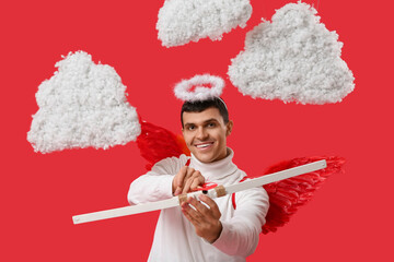 Young man dressed as Cupid with bow in clouds on red background. Valentine's Day celebration
