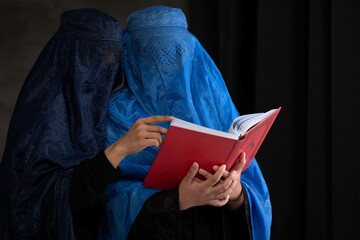 Two Afghan Muslim women with burka tradition cloths in Afghanistan and West Pakistan, studying holy...