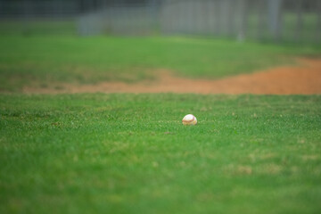 Baseball game, baseball ball siting on the grass on the diamond near the pitcher's mound during the...