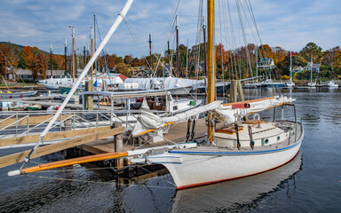Small Sailboat at a New England Dock:  A boat with furled sails sits quietly by a wooden pier on an...