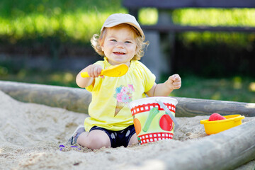 Cute toddler girl playing in sand on outdoor playground. Beautiful baby having fun on sunny warm...
