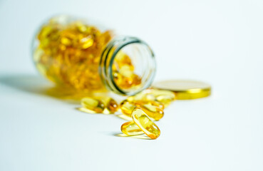 Fish Oil supplement capsules for health spill out from clear glass bottle with golden cap isolated on white background.