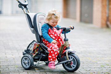 Cute adorable toddler girl sitting on pushing bicycle or tricycle. Little baby child going for a...