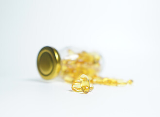 Fish Oil supplement capsules for health spill out from clear glass bottle with golden cap isolated on white background.