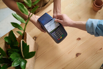 Female cashier receiving cashless payment from client at houseplant store