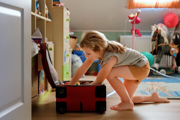Little girl packing suitcase at home. Cute child putting clothes into suitcase. Preparing for...