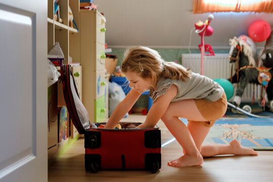 Little girl packing suitcase at home. Cute child putting clothes into suitcase. Preparing for family vacations with children. Practicing independence