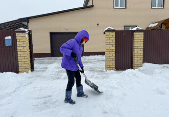 A girl cleans snow with a shovel in the courtyard of the house