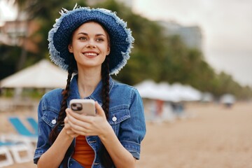 Pretty young woman, stylishly clad in a fashionable hat and casual attire, holding a smartphone and...