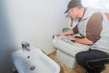 Plumber checks a leaky toilet pipe that has ruined the wall behind the toilet to figure out what...