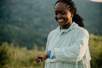 African American woman jogging gracefully in a scenic outdoor setting, checking her smartwatch for fitness progress