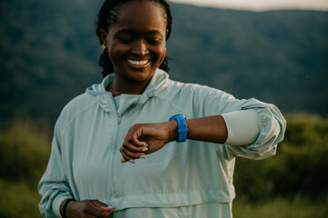 Confident African American woman running outdoors, syncing her pace with a smartwatch for optimal...