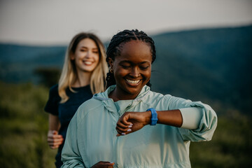 Black and white women jogging together, glancing at smartwatches for fitness updates