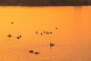 Adventurous people on a stand up paddle board is paddling during a bright and vibrant sunrise
