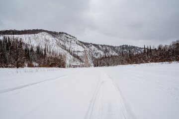 Obraz premium Beautiful winter landscape in cloudy weather, snowmobile tracks in the snow, solo trip to the northern regions of the country, cold winter.