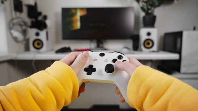 The teenager holds a large white gamepad in his hands and actively presses buttons. Close-up of the hands. First-person view
