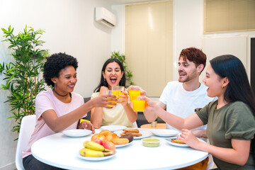 Multi-ethnic friends toasting with orange juice during breakfast