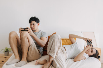Asian Thai couple sitting back to back on sofa at home, Both man and woman using mobile phone, playing game online, ignoring living in apartment room. - obrazy, fototapety, plakaty