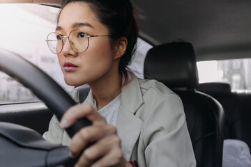 Front view of asian Thai woman staring, holding steering wheel while driving a car on road, going for work in the morning.