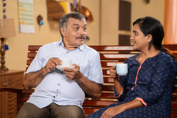 Indian senior retired father with daughter spending time by drinking tea at home - concept of...