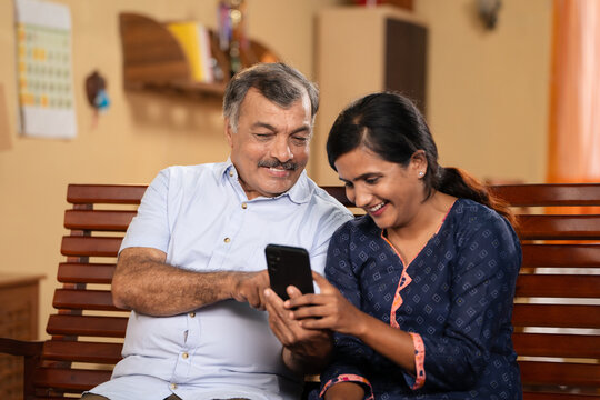 50s Indian father showing proposal photos on mobile phone to daughter for marriage at home - concept of match making, arranged marriage and responsibility