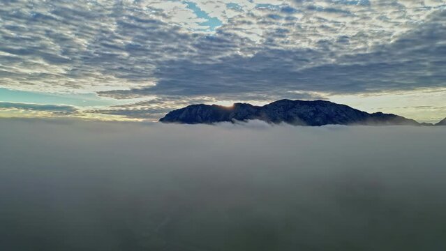 Morning fog moving while the sun shines behind hte high peaks of the Alps in Austria. Drone shot