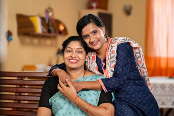 happy smiling Mother with daughter looking at camera by embracing or hugging each other at home -...
