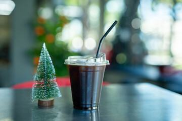 Close-up of Americano iced coffee or black coffee in cup mug and small Christmas tree on wood desk office desk in coffee shop at the cafe in garden,during business work concept