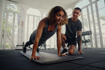 Crédence de cuisine en verre imprimé Fitness Multiracial trainer with young woman in sports clothing doing push-up exercises at the gym