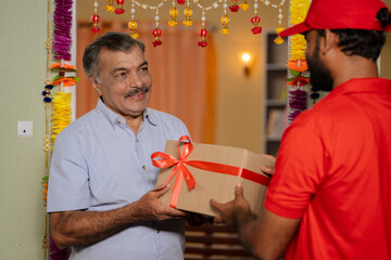 Indian elderly senior man receiving parcel or box from delivery person at home - concept of...
