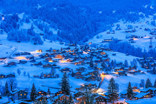 Grindelwald villages with wooden chalets covered with snow in cold winter season at the blue hours in Swiss Alps