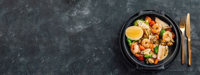 Mixed Seafood Contain Shrimps, Mussels, Calamari Squids and Fish with Broccoli, Cherry Tomato, Lemon on Black dish in restaurant-style platting. Seafood salad on dark background. Top view, copy space