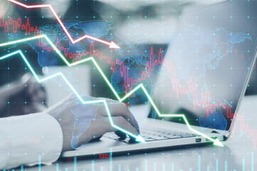 Close up of businessman hands using laptop on desk with falling forex chart arrows on blurry...
