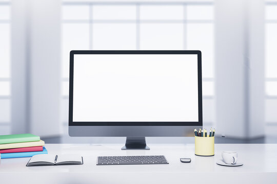 Modern designer desktop with white computer monitor, coffee cup, supplies, other objects and window with city view in the background. Mock up, 3D Rendering.