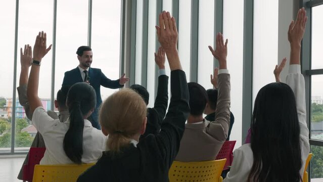 During a conference, a diverse crowd of businesspeople raises their hands to ask questions, vote, or volunteer. This scene emphasizes teamwork and active audience involvement.