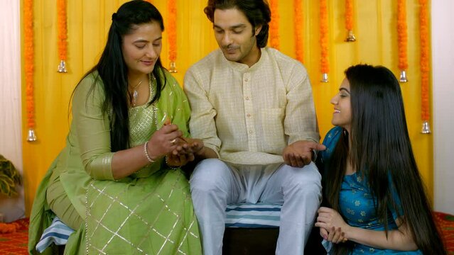 Loving family celebrating Indian wedding ceremony together - Mehendi function  Hindu marriage ritual. Sweet mother applying ethnic henna designs to her son's hand - wedding henna art/tattoo  family...