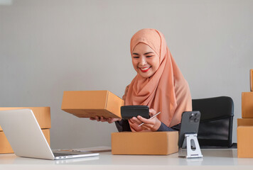 Asian Muslim businesswoman checks stock orders and saves them on her home office laptop. small business owner Shipping in online markets The concept of freedom in life