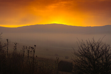 Obraz premium Autumn foggy sunrise. Sunrise photo with a landscape covered in fog, amazing orange sky in the country side.