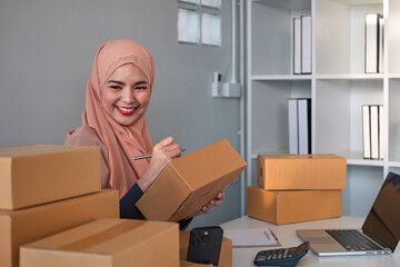 Asian Muslim businesswoman checks stock orders and saves them on her home office laptop. small business owner Shipping in online markets The concept of freedom in life