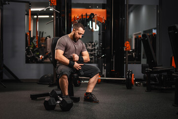 Fototapeta na wymiar A bearded male athlete powerlifter sits at a sports projectile and prepares to lift a barbell. Sports in the gym.