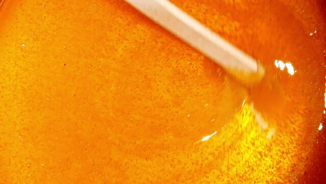 Liquid yellow, gold depilatory wax or sugar paste on a wooden stick close-up. Master mixes the heating wax with a wooden spatula before the depilation waxing procedure. . High quality 4k footage