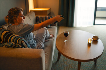 A young woman watches TV in the evening in the cozy living room at home.